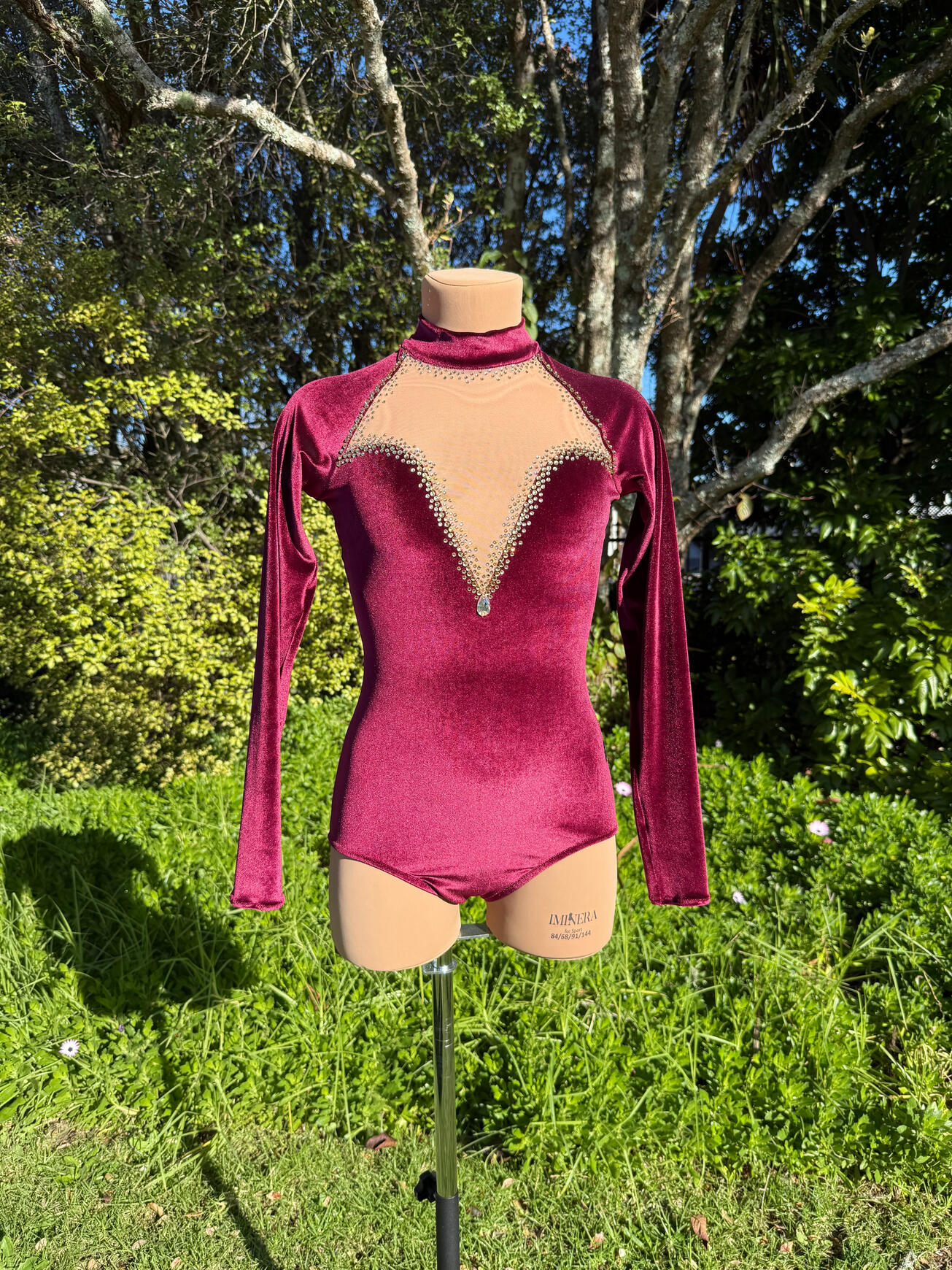 Deep red/burgundy velvet rhythmic gymnastics leotard with gold rhinestones in three shades. Sweetheart neckline in nude mesh with a velvet turtle neck. This is an entry-level custom piece.
